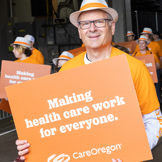 Grupo de personas vestidas de naranja con pancartas en las que se pueden leer "Making health care work for everyone. CareOregon", en un desfile.