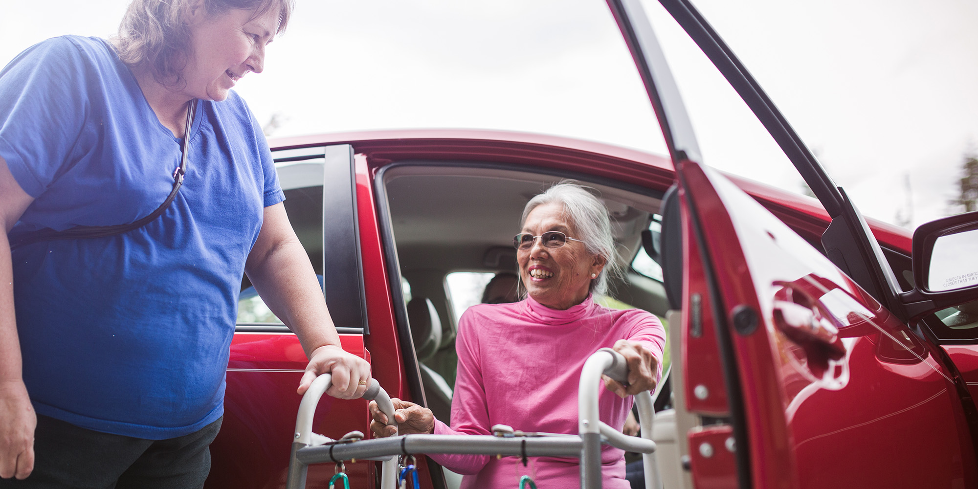 Woman getting out of a car with assistance, using a walker