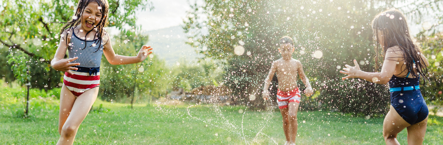 Children playing in a backyard sprinkler on a hot summer day.